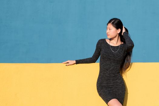 beautiful oriental woman posing in a tight dress on a colorful yellow and blue background, concept of fashion and lifestyle, copyspace for text