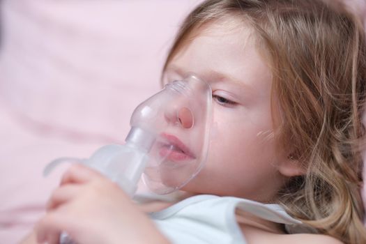 Little baby girl with oxygen mask lying on hospital bed or at home. Upset sad sick child breathing oxygen mask concept