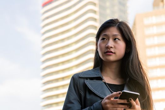 young asian woman consulting her cell phone in the downtown, technology and urban lifestyle concept, copy space for text