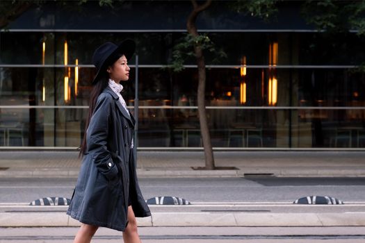 beautiful asian woman in hat and trench coat walking in the city, concept of elegance and urban lifestyle, copy space for text