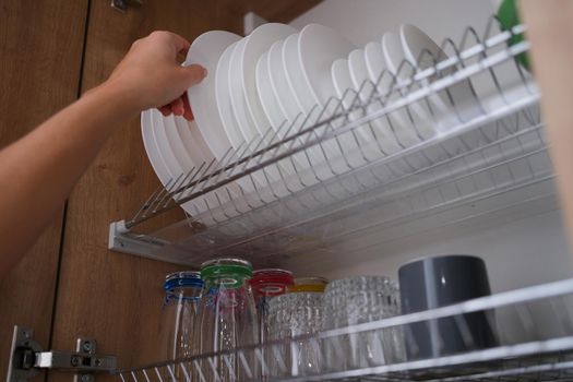 Woman graceful hand takes out clean plate from cupboard. Dryer for dishes in closet concept