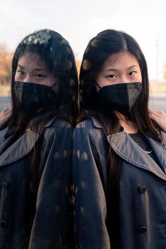 vertical portrait of an oriental woman wearing a black protective mask reflected in a mirror, concept of protection against pollution and viruses