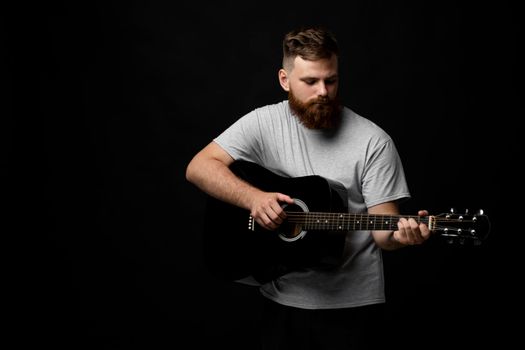 Portraite of handsome brunette bearded man musician, guitarist standing and holding a acoustic guitar in a hand