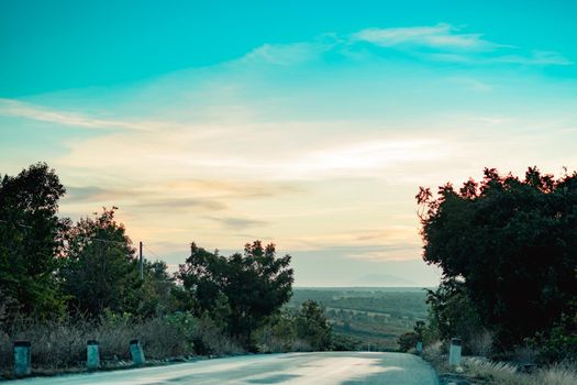 Natural landscape scenery, curvy road into the distance towards green endless hills at sunset dusk against pink sky clouds. Rest journey.