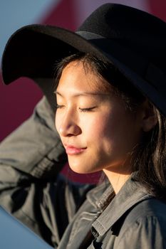 inspirational portrait of a beautiful young chinese woman enjoying the sun on her face with eyes closed, fashion and lifestyle concept, copy space for text