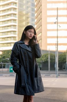 vertical photo of a young asian woman talking by mobile phone while walking in the city, technology and urban lifestyle concept, copy space for text