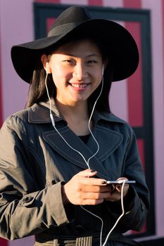 vertical portrait of a smiling beautiful classy chinese woman with earphones listening music from her phone, concept of technology and fashion lifestyle