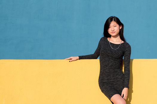 beautiful smiling asian woman in a tight dress on a colorful yellow and blue background, concept of fashion and lifestyle, copyspace for text