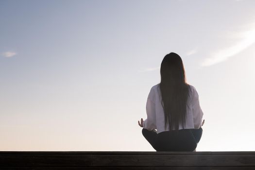 rear view of a young woman with long hair meditating at sunrise, concept of relaxation and mental health, copy space for text