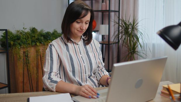 Young business woman freelancer at the home office room, sits down to desk, opens laptop. Girl student works on notebook, sends messages, makes online purchases, study, e-learning, remote job