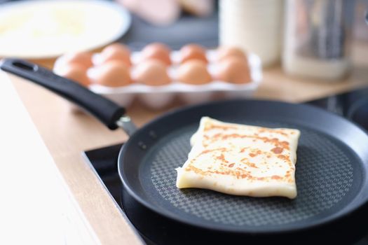 Folded pancake in frying pan against background of chicken eggs in kitchen. Spring rolls and delicious recipes concept
