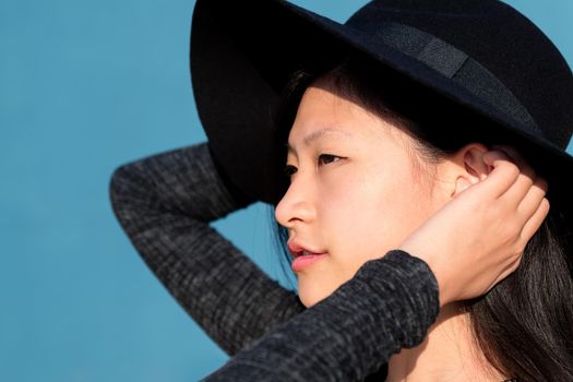 profile portrait of an elegant and beautiful asian woman in a hat on blue background, concept of fashion and lifestyle, copyspace for text