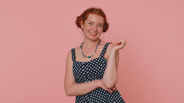 Cheerful lovely redhead young woman in black dress smiling, looking at camera, flirting. Adult fashion red hair model girl indoors studio shot isolated on pink background. Female nature beauty