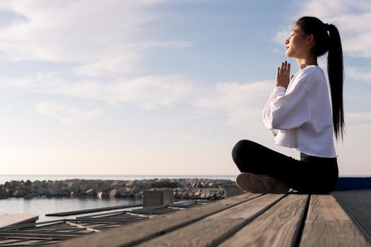 young asian woman sitting meditating by the sea at sunrise, relaxation and mental health concept, copyspace for text