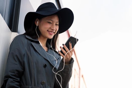 happy young asian woman with earphones making a video call with her smart phone, concept of technology and modern lifestyle, copyspace for text