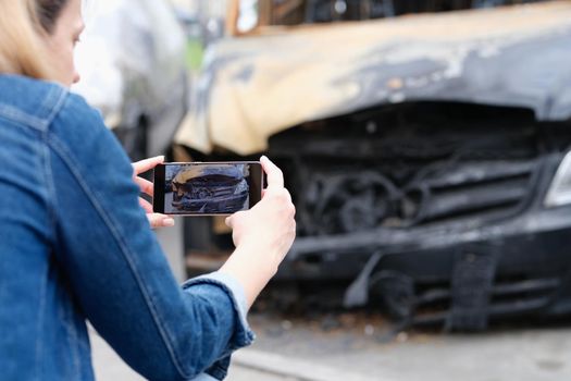 Woman insurance agent or reporter journalist taking pictures of burnt car. Car arson and crime concept