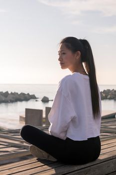 young asian woman sitting relaxed after meditate by the sea at sunrise, relaxation and mental health concept, copyspace for text