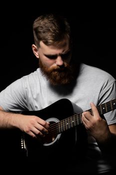 Bearded brutal guitarist plays an acoustic guitar in a black room