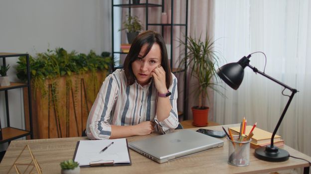 Young woman businesswoman analyzing documents reading contract invoices or graphics report and working on laptop sitting at home office table desk. Girl freelancer study, remote job e-learning online
