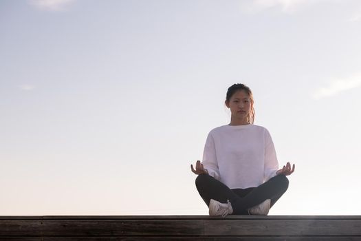 young oriental woman sitting meditating at sunrise, concept of relaxation and mental health, copy space for text