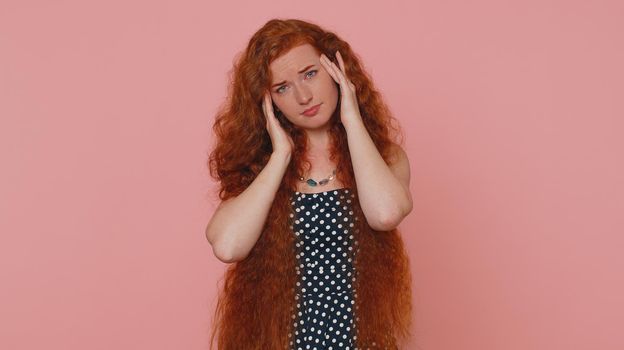 Redhead sleepy young woman in dress rubbing temples to cure headache problem, suffering from tension and migaine, stress, grimacing in pain, high blood pressure. Girl isolated alone on pink background