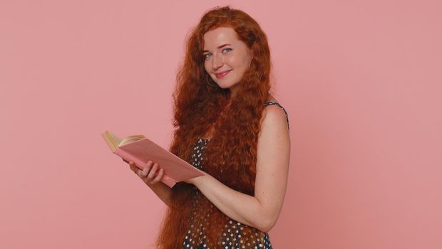 Redhead young woman reading funny interesting fairytale story book, leisure hobby, knowledge wisdom, education, learning, study, wow. Red hair ginger freckles girl isolated on pink studio background