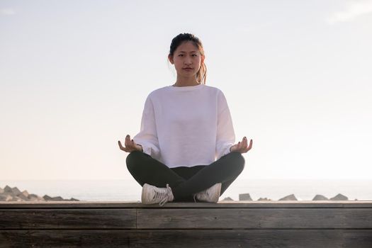 young asian woman sitting meditating at sunrise, concept of relaxation and mental health, copy space for text