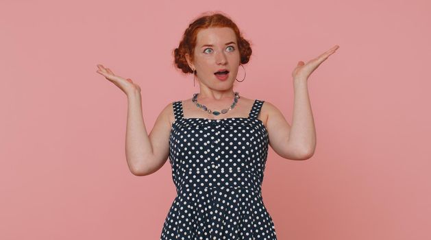 Excited amazed ginger woman in polkadot dress touching head, showing explosion, looking worried and shocked, professional burnout. Looking surprised wow girl isolated alone on pink studio background