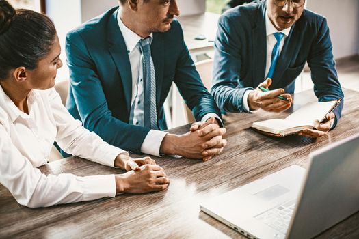 Business Group Brainstorming While Sitting At Office Desk, Colleagues Listen To Speaker, Intelligent Man Explaining Business Development Strategy While Looking In Notebook, Cropped Shot, Toned Image