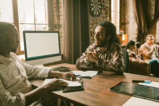 Teamwork Of International Team, Creative People Communication In Modern Interior Of Coworking Space, Young African And Arab Men Talks Sitting At Table, Some People Discussion On Blurred Background