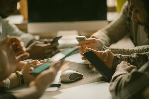 Group Of Young People Using Smart Phones, Close Up Of Human Hands Holding Mobile Phones While Sitting At Office Table Near Window, Side View