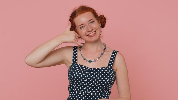 Call us, here is contact number. Redhead young woman seller looking at camera doing phone gesture like says hey you call me back. Adult ginger girl indoors studio shot isolated on pink background