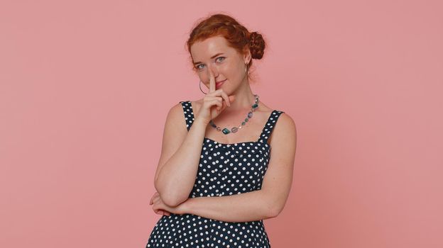 Shh be quiet please. Portrait of redhead woman 20s presses index finger to lips makes silence gesture sign do not tells secret. Young beautiful ginger girl posing isolated on pink studio background