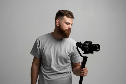 Videographer making a good footage using steadicam. Cameraman creator with a stabilizer in his hands takes a video on the slr video camera on white background. Creating a video content