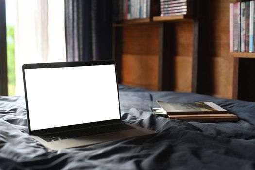 Laptop and books in comfortable bed with soft light from window. Blank screen for advertise text.