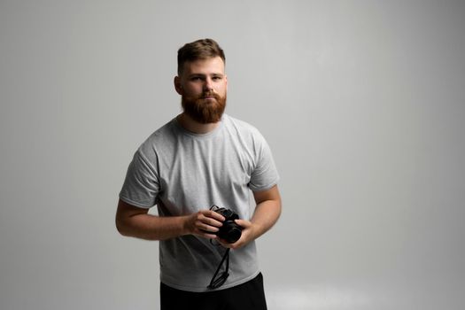 Young bearded proffesional photographer man with a dslr camera over white background