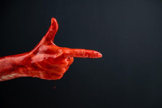 Woman's hand in blood shows a gesture of a gun on a black background