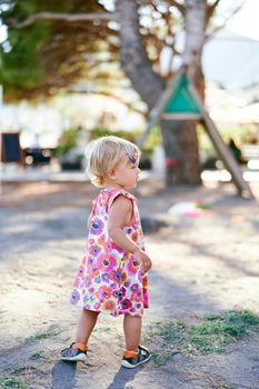 Little girl stands on the playground and looks away. High quality photo