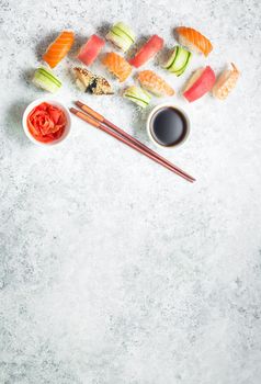 Assorted sushi set on white concrete background. Space for text. Japanese sushi, rolls, soy sauce, ginger, chopsticks. Top view. Sushi nigiri. Japanese dinner/lunch. Food frame. Different sushi mixed