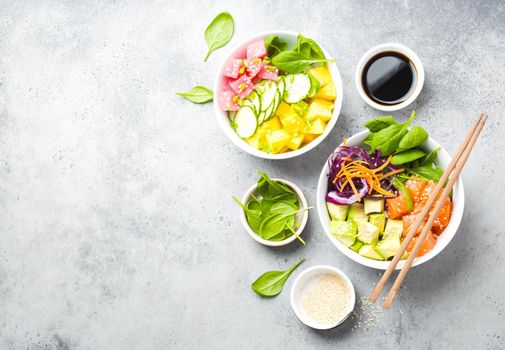 Two assorted poke bowls with raw fish and vegetables, space for text. Top view. Traditional Hawaiian dish, rustic stone background. Healthy clean eating concept. Poke with raw fish slices, copy space