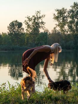 Beautiful woman enjoys holidays at sunset near river with pets company