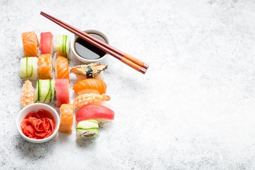 Assorted sushi set on white concrete background. Space for text. Japanese sushi, rolls, soy sauce, ginger, chopsticks. Top view. Sushi nigiri. Japanese dinner/lunch. Food frame. Different sushi mixed