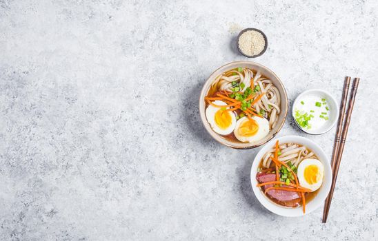 Bowls with Japanese soup ramen, chopsticks, white concrete rustic background. Traditional Asian soup with noodles, meat, eggs. Asian food. Japanese ramen for dinner. Space for text. Ramen, top view