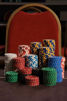 Close-up shot of a poker chips standing on a table against a red chair in casino. Gambling, fortune, game and entertainment concept.