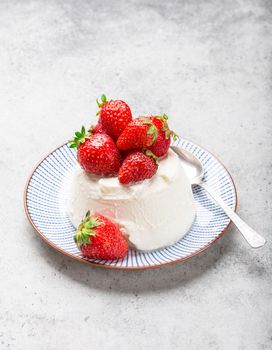 Fresh Italian cheese ricotta with strawberries on a plate with a spoon, grey rustic stone background, light summer dessert or snack, good for diet or healthy eating. Selective focus, close-up