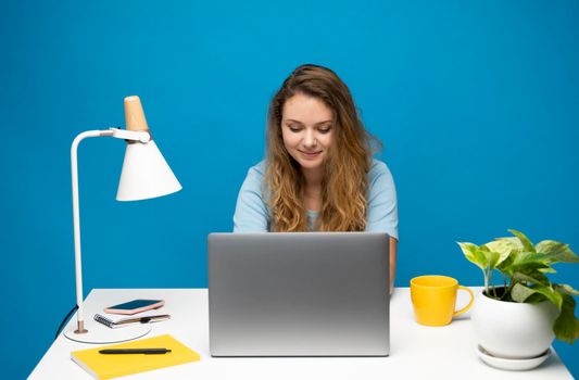 Young freelancer curly woman in a blue t-shirt working with a laptop computer. Working on a project. Freelance worker