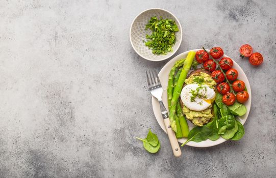 Healthy vegetarian meal plate. Toast, avocado, poached egg, asparagus, baked tomatoes, spinach. Stone background. Space for text. Vegetarian breakfast plate. Diet. Organic clean healthy food. Top view