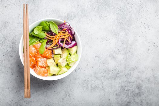 Top view of poke bowl with fresh raw salmon and vegetables, space for text. Traditional Hawaiian dish on rustic stone background. Healthy and clean eating concept. Poke with slices of fish, copy space