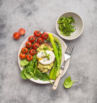Healthy vegetarian meal plate. Toast, avocado, poached egg, asparagus, baked tomatoes, spinach. Stone background. Vegetarian breakfast plate. Clean healthy eating. Diet. Organic healthy food. Top view