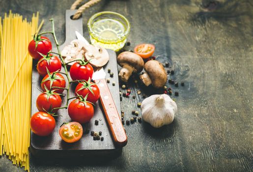 Cherry tomatoes, mushrooms, spaghetti, wooden cutting board, knife. Garlic, olive oil. Cooking background. Space for text. Ingredients for cooking. Cooking dinner. Selective focus. Food background